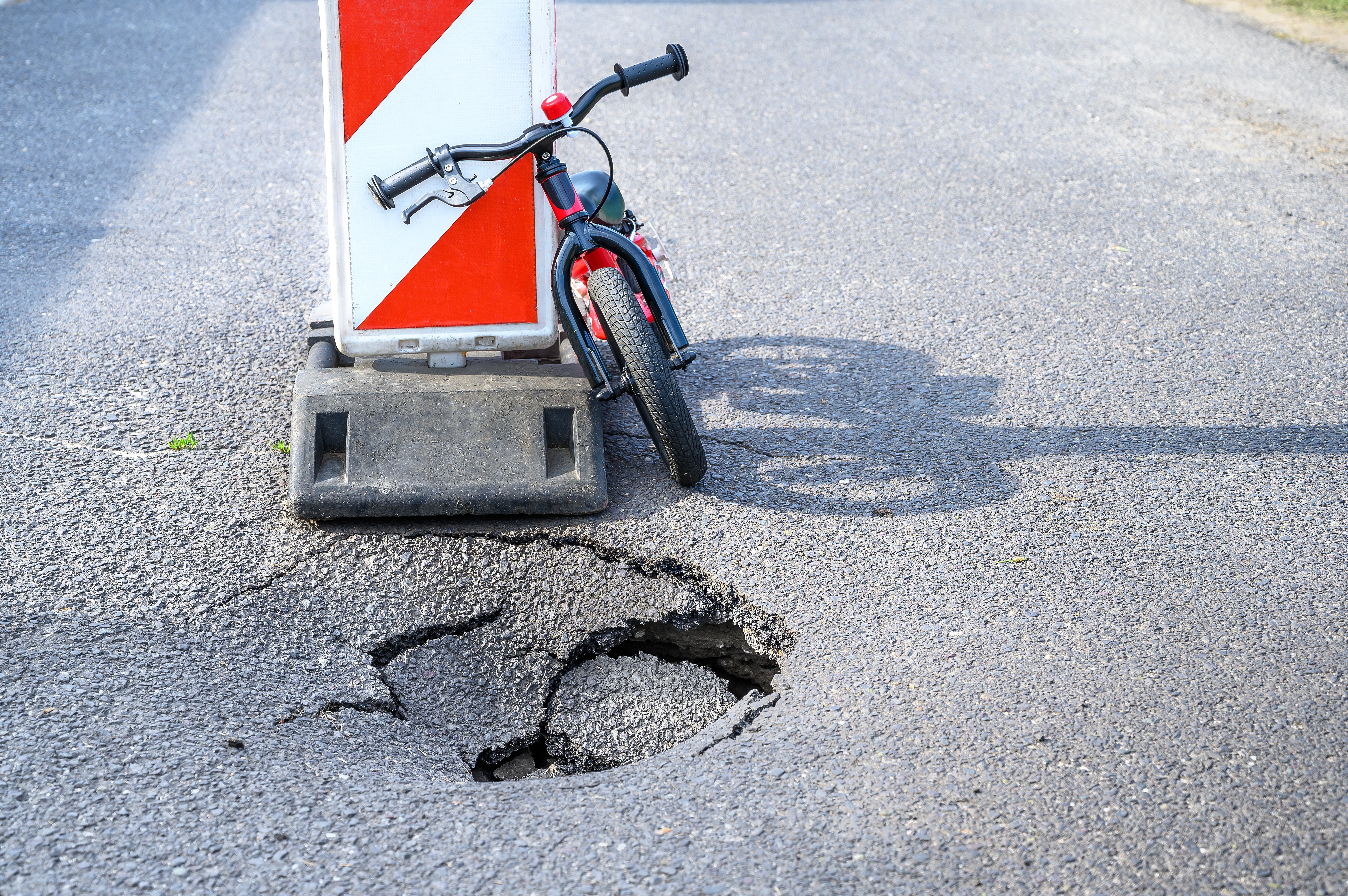 Ein Kinderfahrrad steht vor einem Schlagloch auf der Straße neben einem Warn Aufsteller