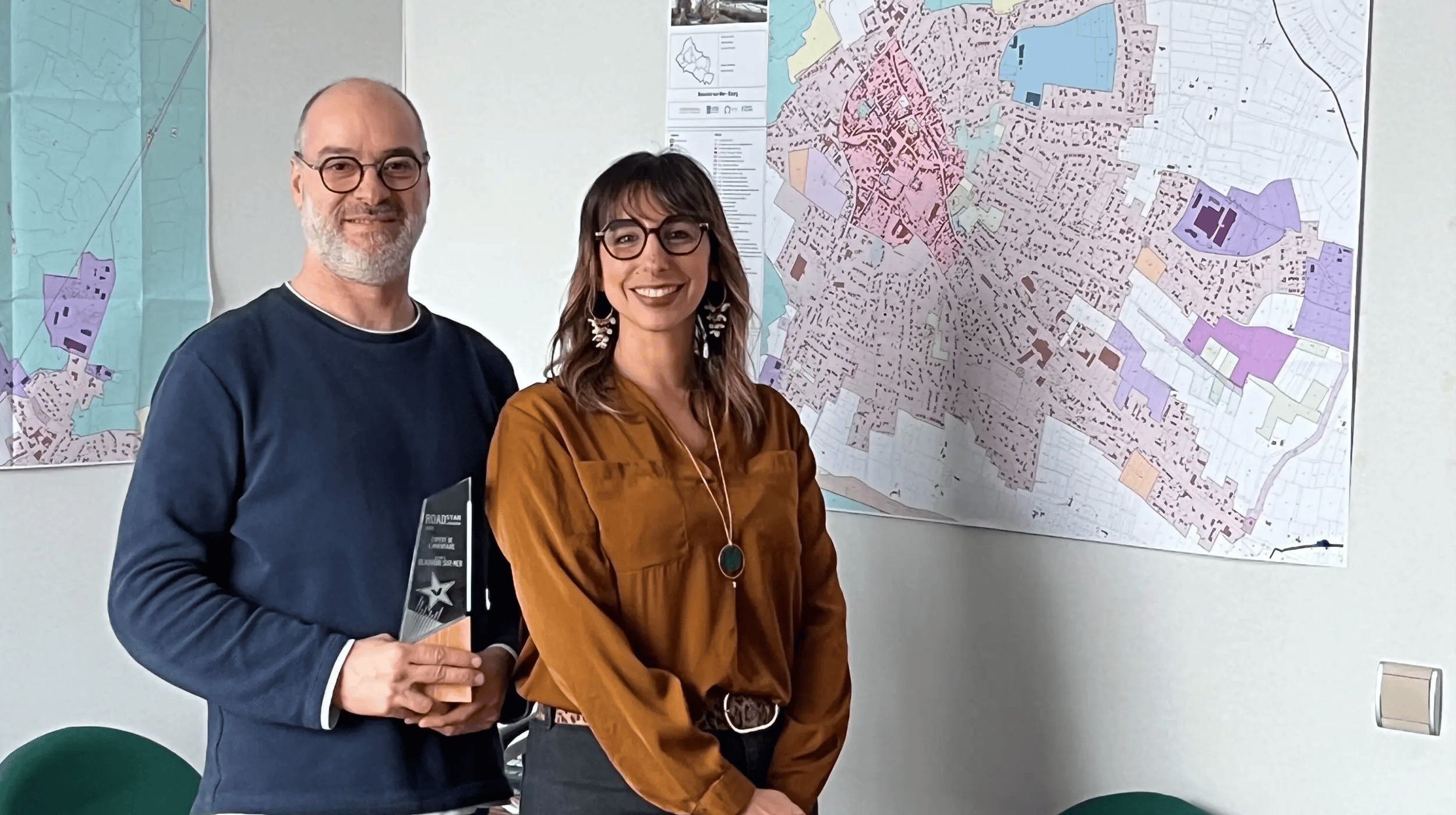 Deux représentants de la commune de Beauvoir-sur-Mer posant fièrement avec leur trophée RoadStar Award 2025 devant une carte de la ville.