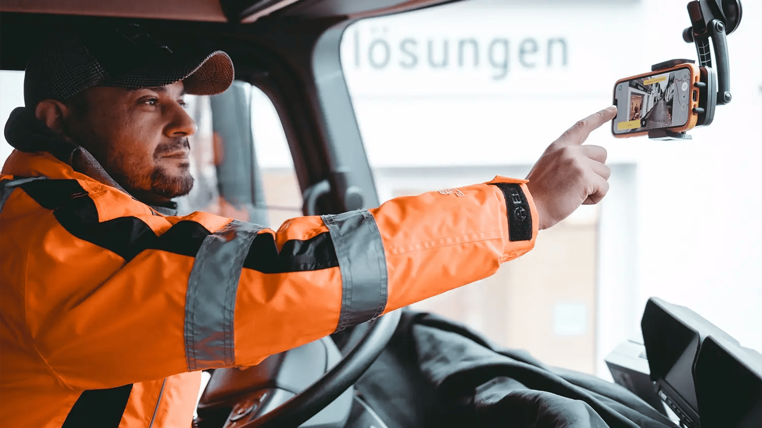 Ein Mann sitzt in einem kommunalen Fahrzeug. Er führt eine Befahrung durch und nutzt die vialytics App auf dem Smartphone an der Windschutzscheibe.